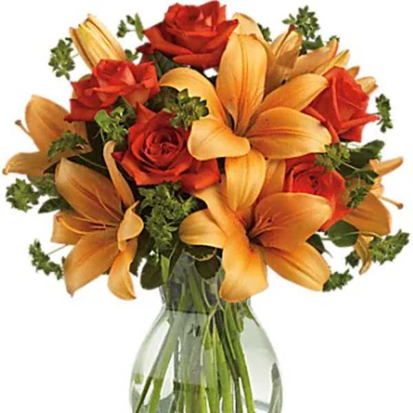 Orange lilies and red roses arranged in a clear glass vase.