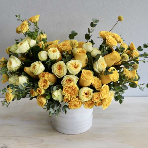 Low arrangement of yellow and cream roses in a white ceramic vase