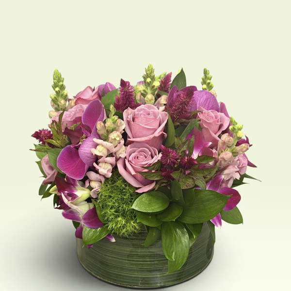 Pink roses and purple orchids arranged in a low green vase