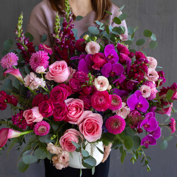 Large bouquet of pink roses, magenta blooms, and purple orchids in a white vase