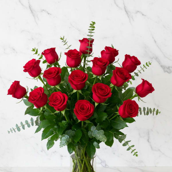 Red roses arranged in a clear glass vase with greenery