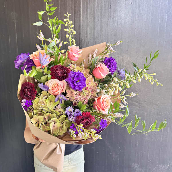 Large bouquet of pink, purple, and green flowers wrapped in brown paper