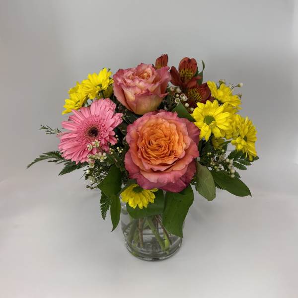 Mixed bouquet of pink and orange roses with yellow daisies in a glass vase
