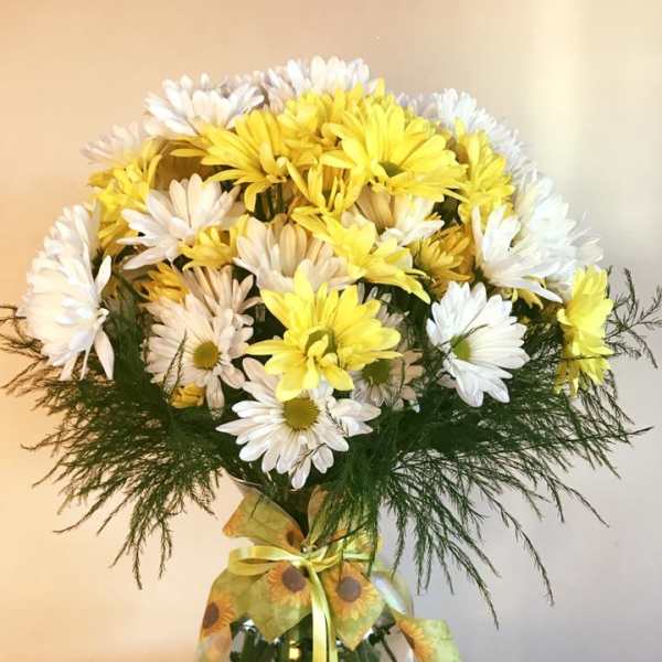 Yellow and white daisy bouquet in a glass vase with a ribbon