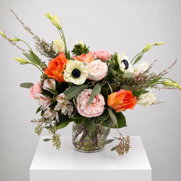 Mixed bouquet of orange, pink, and white flowers in a clear glass vase