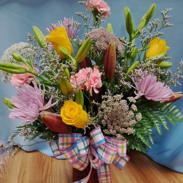 Mixed bouquet with yellow roses, pink lilies, and a plaid ribbon in a vase