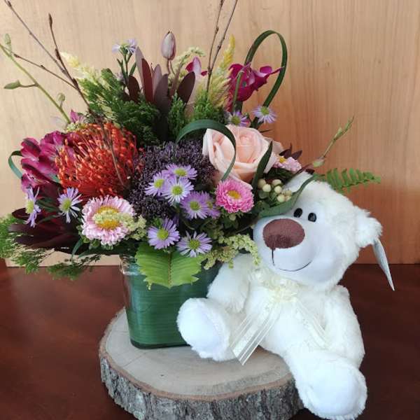 Mixed flower arrangement in a green vase with a white teddy bear