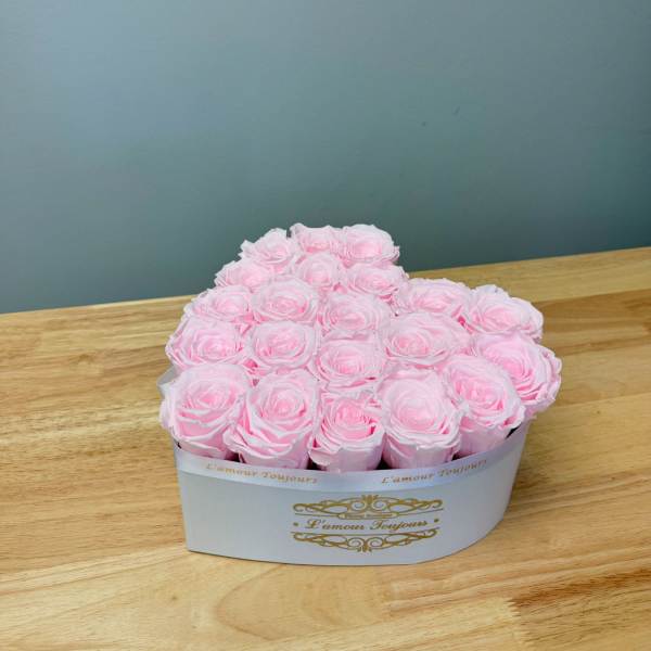 Pink roses arranged in a white heart-shaped box on a wooden table