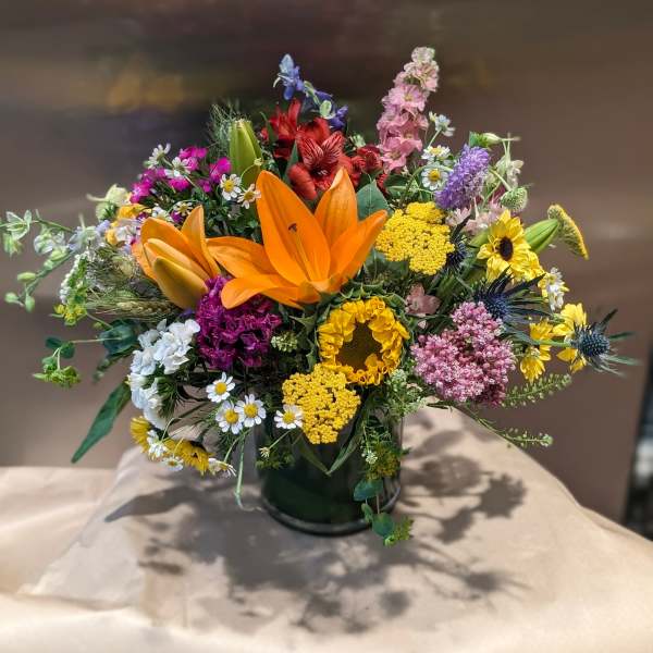 Colorful mixed bouquet with orange lilies and sunflowers in a dark vase