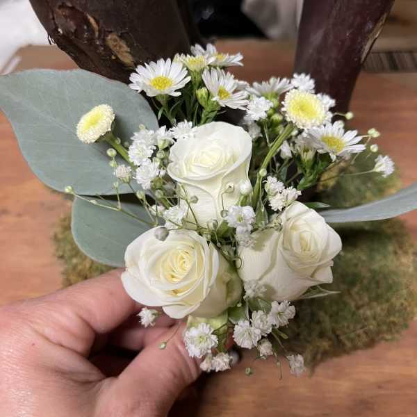 Small wedding boutonniere with white roses, tiny white daisies, and filler blooms held in a hand