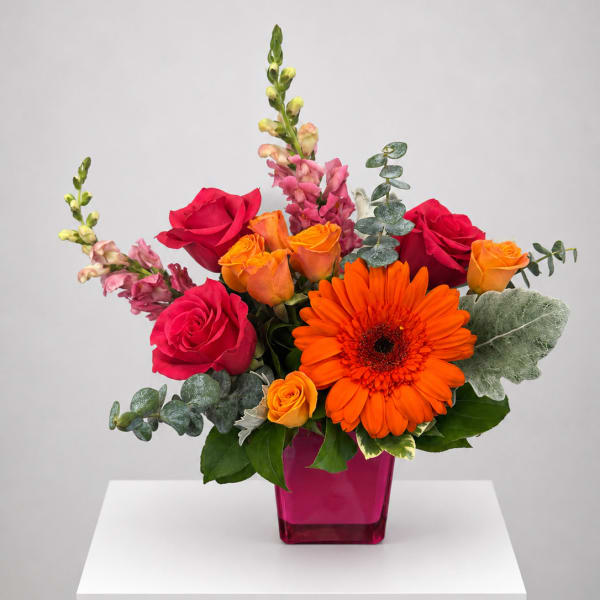 Bouquet of red and orange roses with a bright orange gerbera in a pink vase