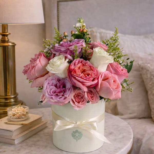 Pink and white roses arranged in a round white box with a ribbon