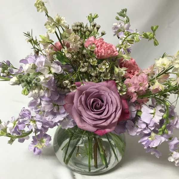 Lavender rose bouquet with pink and white flowers in a round glass vase