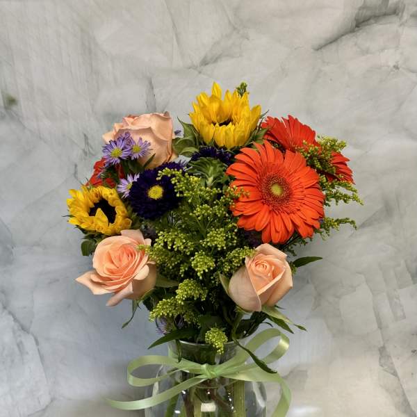 Mixed bouquet of roses, gerbera daisies, and sunflowers in a glass vase