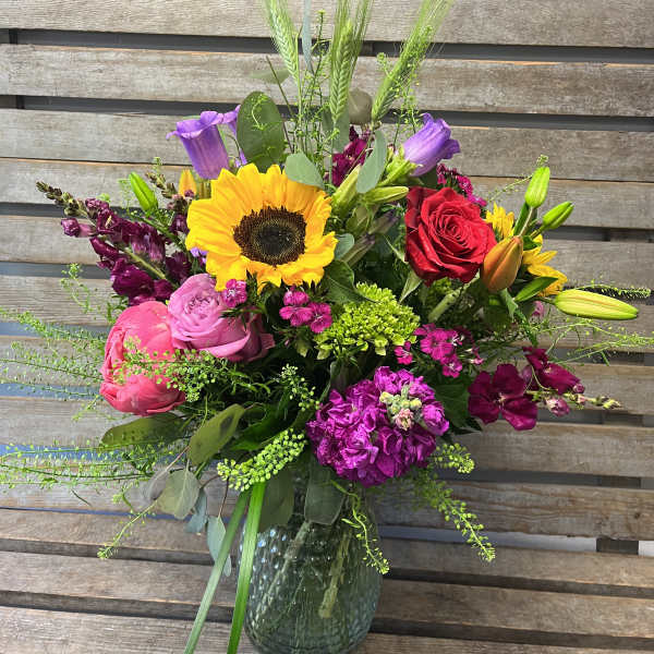 Mixed bouquet in a glass vase with a sunflower, roses, lilies, and purple blooms