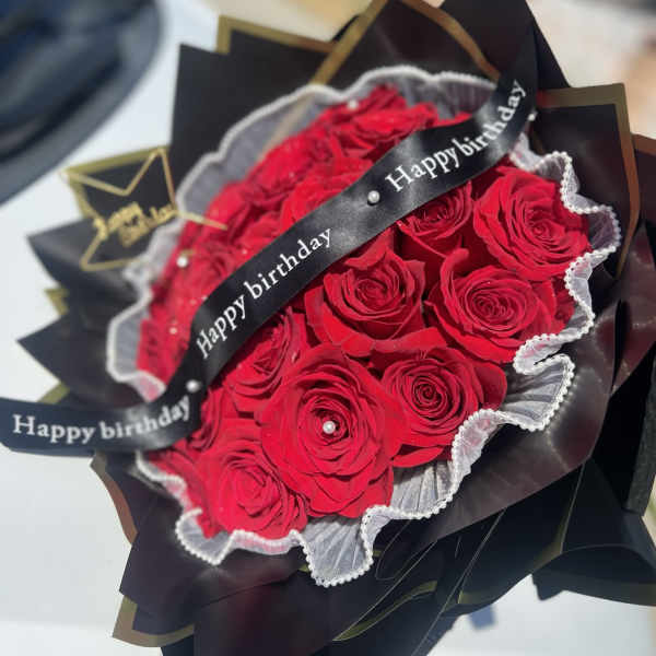 Bouquet of red roses wrapped in black paper with a birthday ribbon