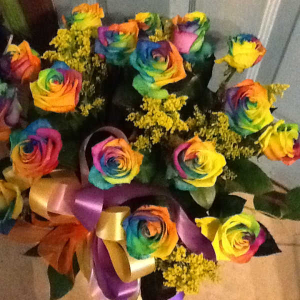 Bouquet of rainbow-colored roses with yellow filler flowers and satin ribbons