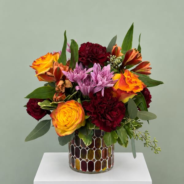 Mixed bouquet of orange roses, purple chrysanthemums, and burgundy carnations in a mosaic vase