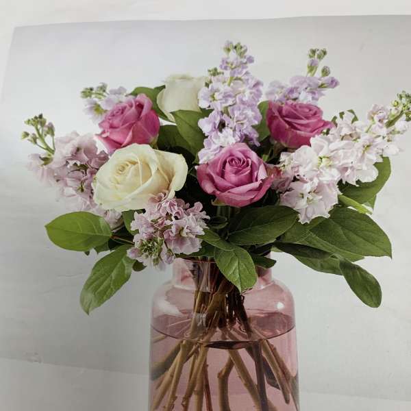 Pink and white roses with lavender blooms in a pink glass vase