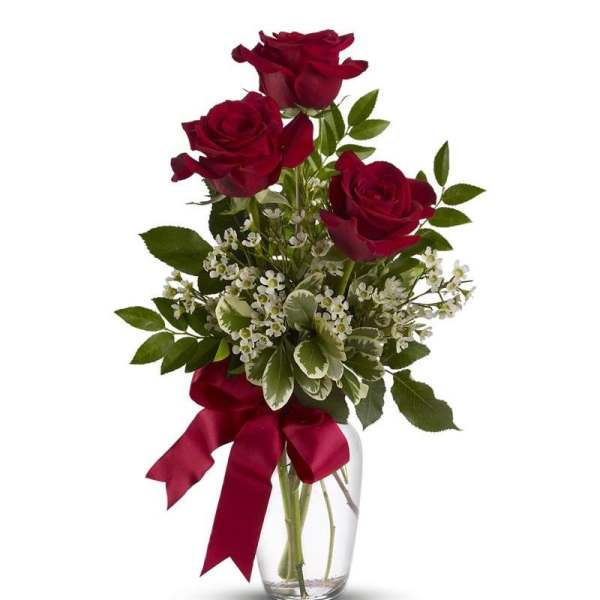 Three red roses in a clear glass vase with a burgundy ribbon