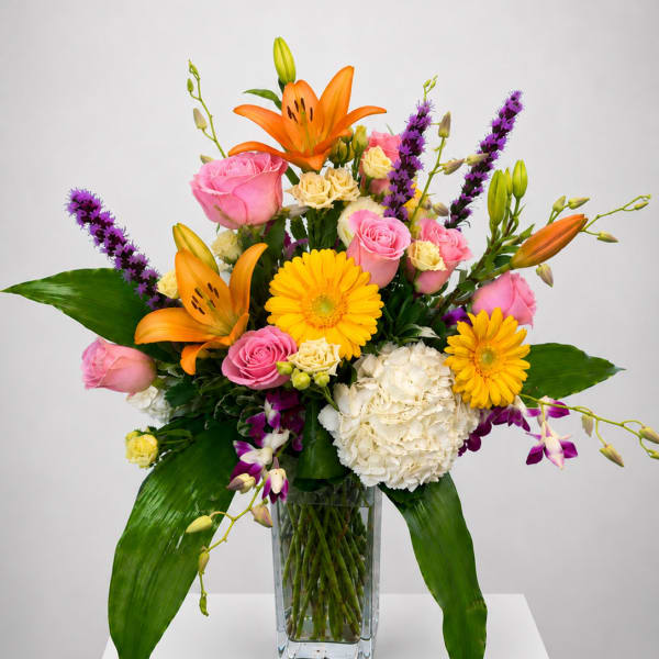 Mixed bouquet of orange lilies, pink roses, and yellow daisies in a glass vase