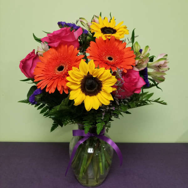 Bouquet of sunflowers, gerbera daisies, and pink roses in a glass vase