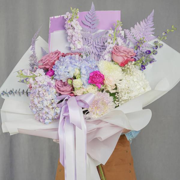 Pastel bouquet of hydrangeas, roses, and chrysanthemums wrapped in white paper