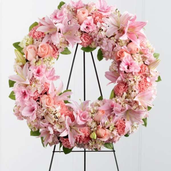 Pink floral wreath on a black stand with lilies and roses