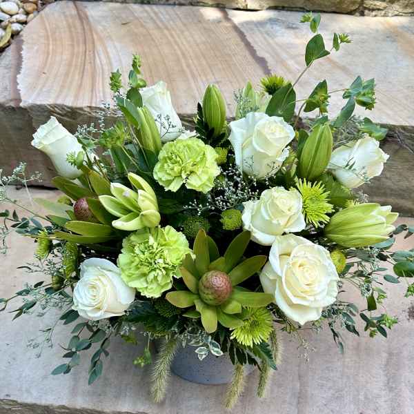 White roses and green flowers arranged in a low vase