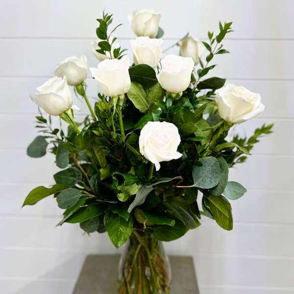 White roses arranged in a clear glass vase with mixed greenery