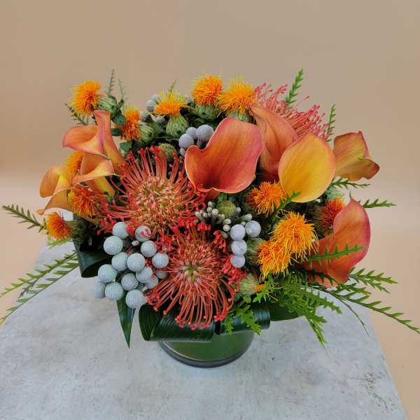 Orange calla lilies and pincushion flowers in a glass vase