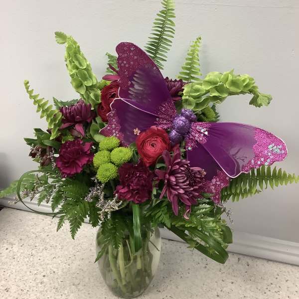 Purple butterfly decoration in a mixed flower bouquet in a glass vase