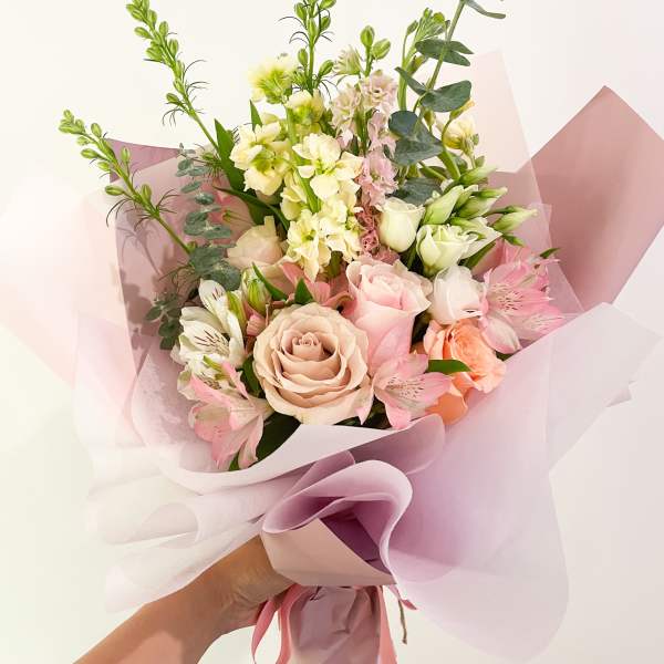 Handheld bouquet of pink and cream roses with pale filler flowers