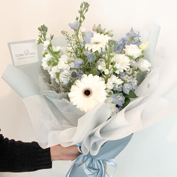 Bouquet of white gerbera daisies and pale blue flowers wrapped in white paper