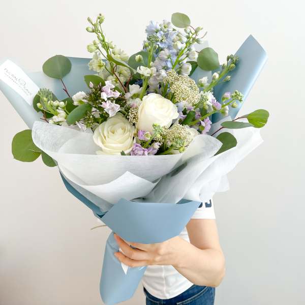 Bouquet of white roses and pastel flowers wrapped in blue and white paper