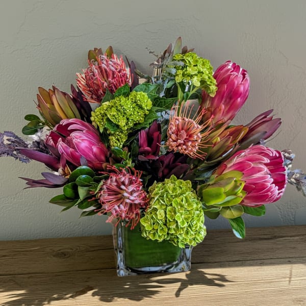 Pink protea and green hydrangea arrangement in a clear square vase