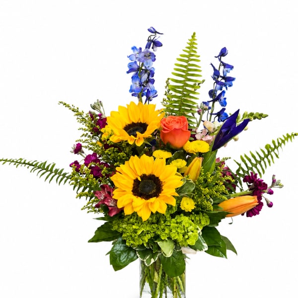 Bright mixed bouquet with sunflowers, roses, and blue flowers in a glass vase