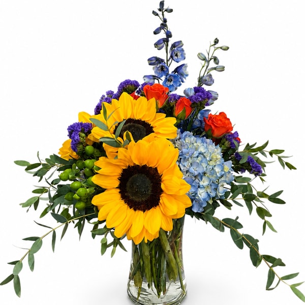 Bouquet of sunflowers, blue hydrangea, orange roses, and purple flowers in a glass vase