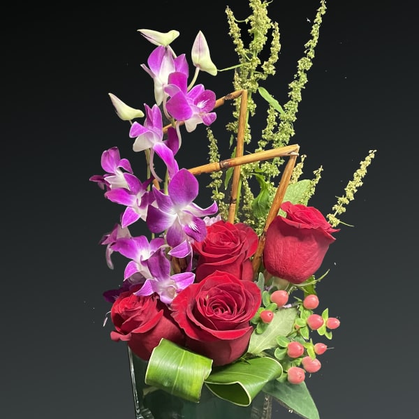 Red roses and purple orchids in a square glass vase