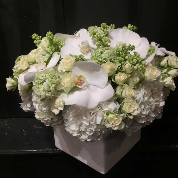 White floral arrangement in a square vase with orchids and roses