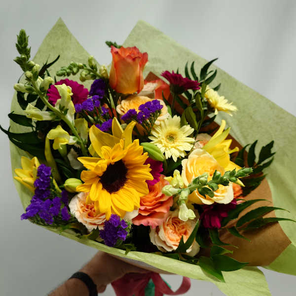 Mixed bouquet with sunflowers, roses, and purple filler flowers wrapped in paper