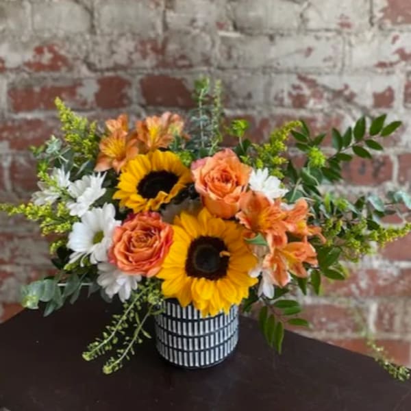 Bouquet of sunflowers, orange roses, and white daisies in a striped vase