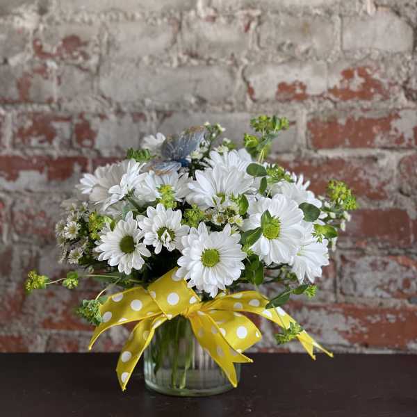 White daisy bouquet in a glass vase with a yellow polka-dot ribbon