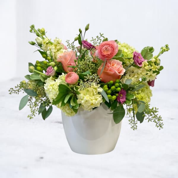 Bouquet of peach roses and green-white blooms in a white vase