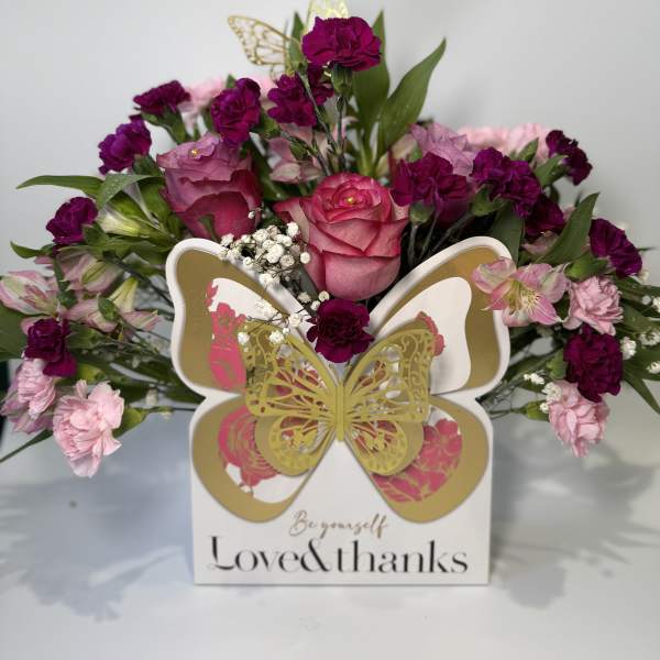 Pink and magenta floral arrangement in a decorative box with butterfly accents