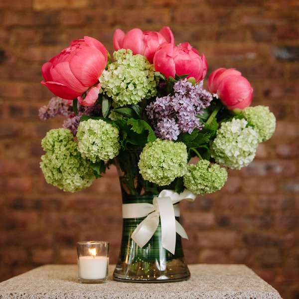 Pink tulips and hydrangeas in a glass vase with a white ribbon