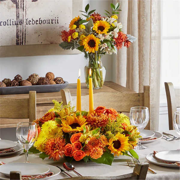 Sunflower and orange floral centerpiece with tall candles on a dining table