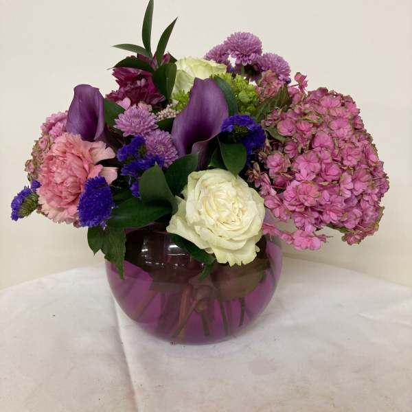 Mixed bouquet of pink, purple, and white flowers in a purple glass vase