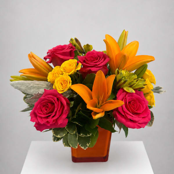 Bouquet of pink roses, yellow spray roses, and orange lilies in an amber vase