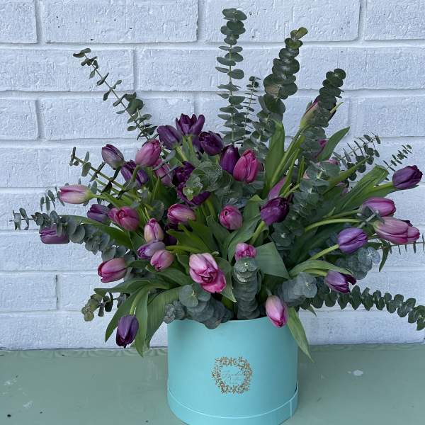 Purple tulips arranged in a turquoise hat box with eucalyptus